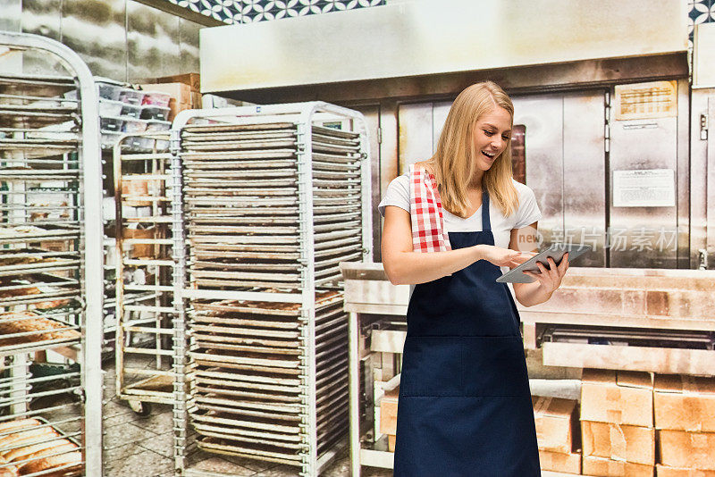 微笑的女面包师在面包店使用平板电脑