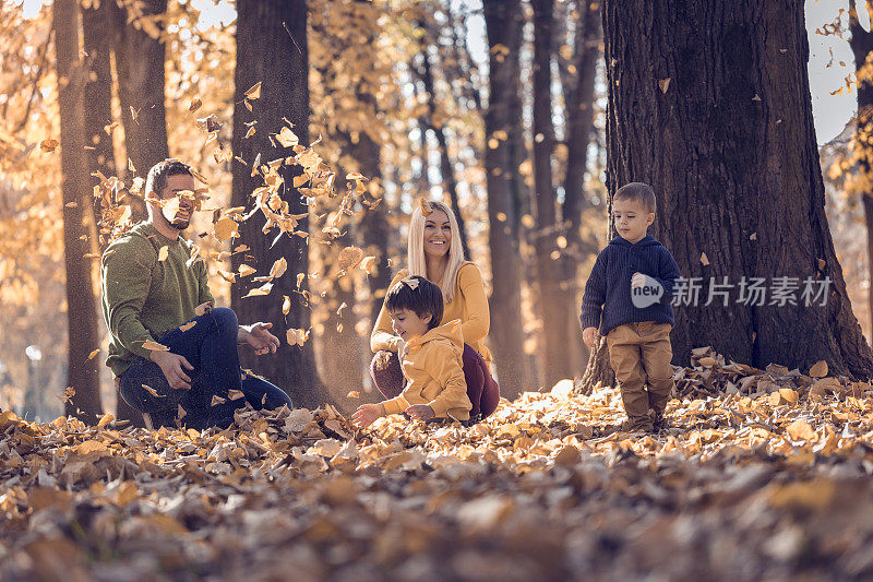 一对快乐的夫妇和两个小男孩在公园里玩秋天的树叶