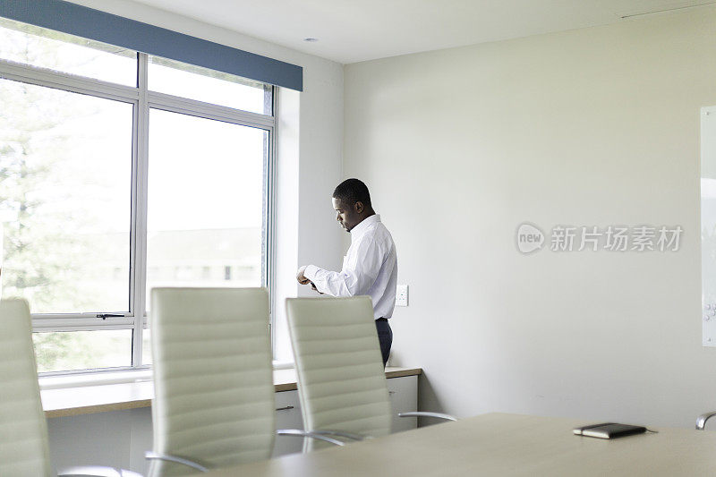 一个非洲商人站在会议室的窗户边