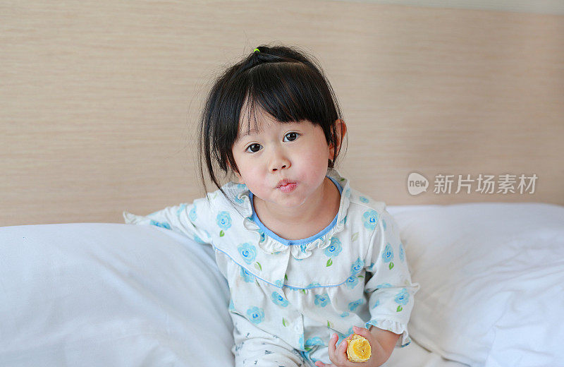 可爱的小女孩早上穿着睡衣在床上吃香蕉。