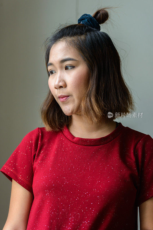 年轻的亚洲妇女穿着红色衬衫连衣裙在房间里望着窗外