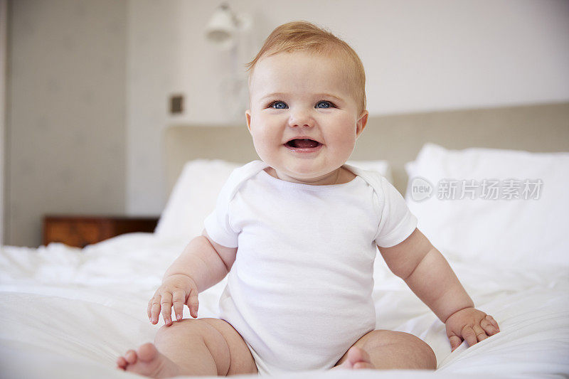 快乐的男婴坐在父母的床上
