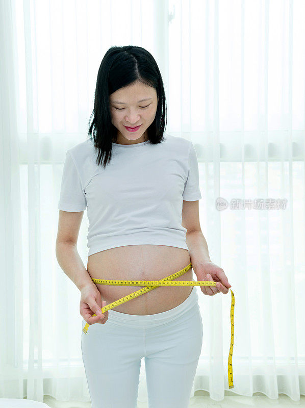 一名孕妇用卷尺测量自己的腹部