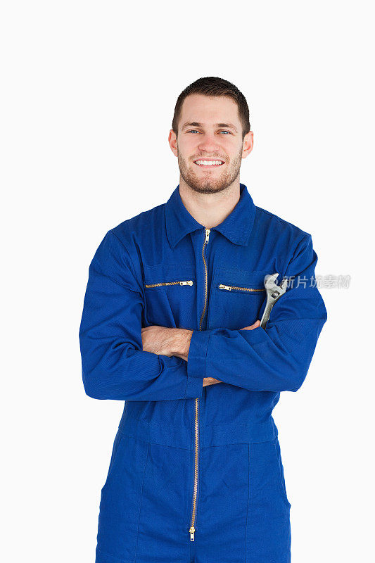 微笑的年轻技工穿着连衫裤，扳手和双臂折叠