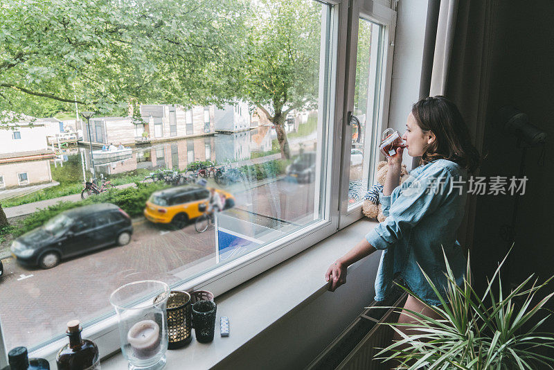 在鹿特丹，一个女人一边喝茶，一边透过窗户望着街道