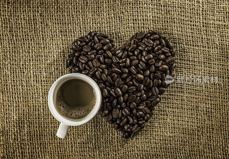 一杯玛奇朵咖啡，用烘培的生咖啡豆在黄麻的背景上做成心形