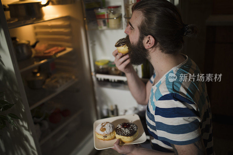 大胡子男人在冰箱前吃甜甜圈