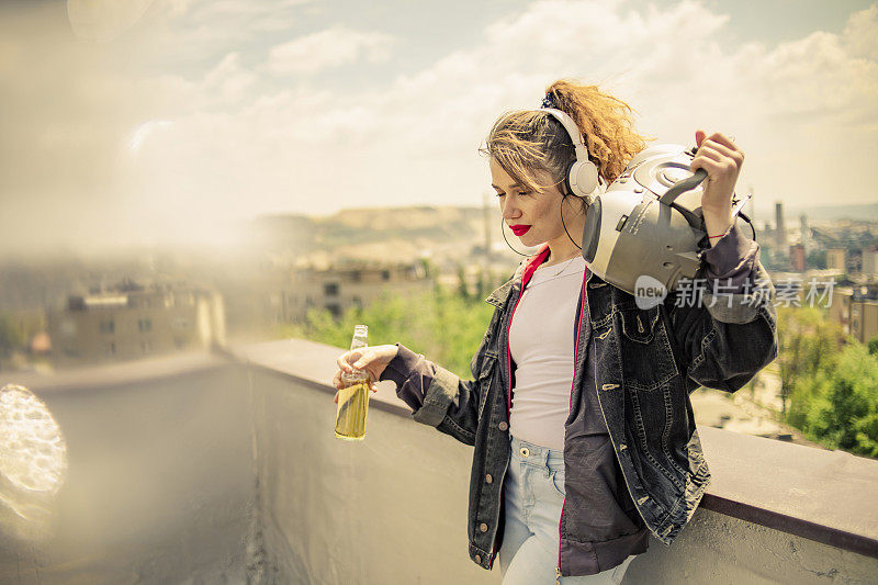 一个年轻的复古风格的女孩在楼顶听音乐-他在楼顶听音乐，享受自由，喝酒