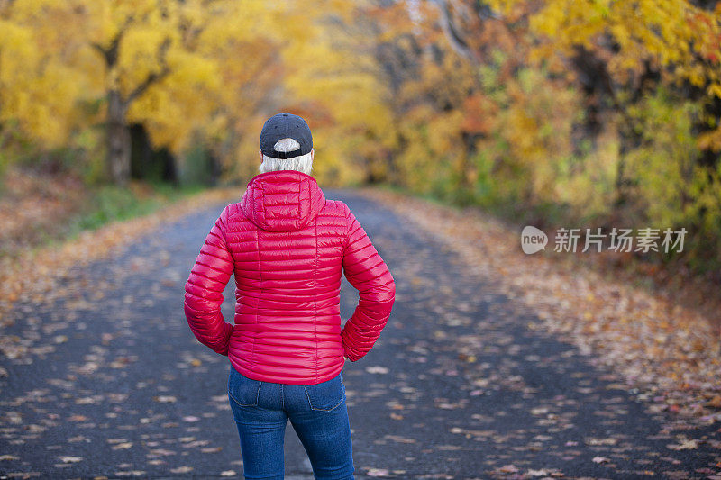 一个女人在路上看着秋天的树叶。