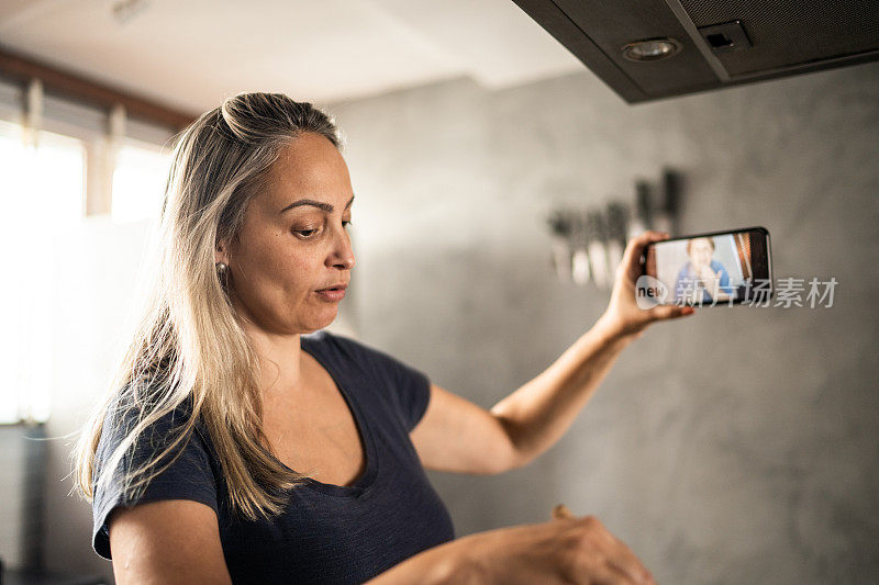 成熟的女人做饭和展示食物在视频通话在家里的智能手机