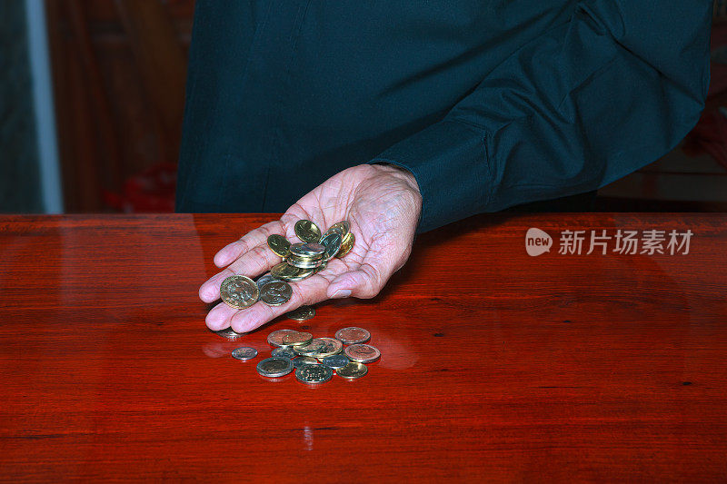 哥伦比亚奖获奖硬币的特写从一个73岁的亚洲印度男性的左手溢出，在一个闪亮的，抛光的，带有丰富的木纹和反射的红木桌面上。硬币几乎在造币厂条件;副本的空间。