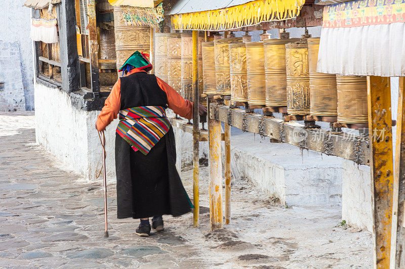 一位藏族老妇人走过经幡鼓，用右手敲了敲