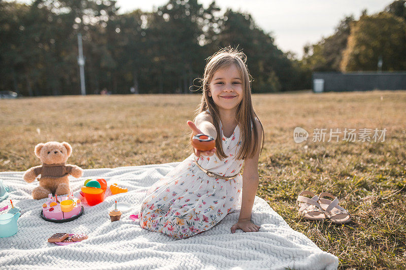 微笑的女孩和她的泰迪熊玩玩具在公园野餐