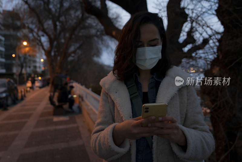 女性游客在城市夜间佩戴防护口罩并使用智能手机