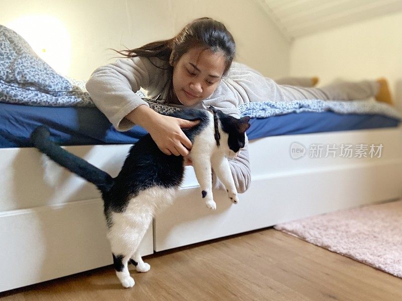 年轻的亚洲女人放松在卧室和猫