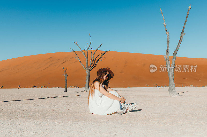 穿着衣服的女人旅行者在纳米比亚的Deadvlei沙漠中部探索风景优美的树木区域