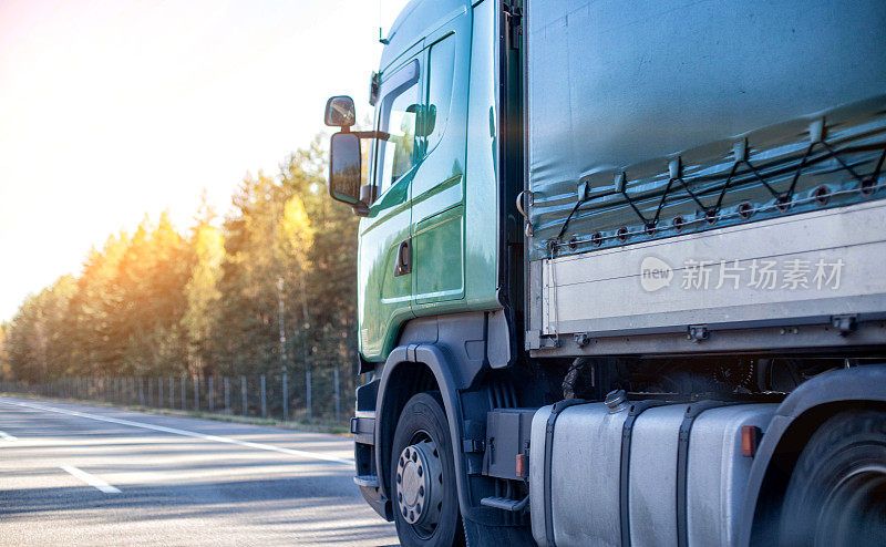 一辆带拖车的现代绿色卡车在阳光明媚的天气里沿着高速公路运送货物。根据里程计算卡车司机工资的概念。文本的复制空间
