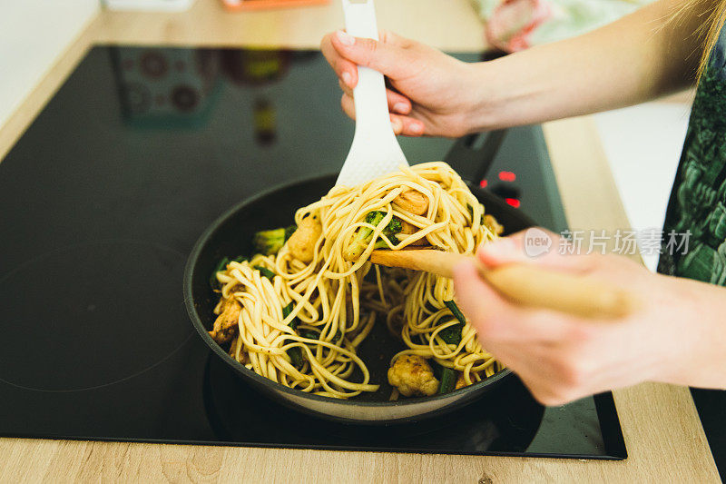 在厨房的锅里，一个女人用鸡肉和蔬菜煮面条