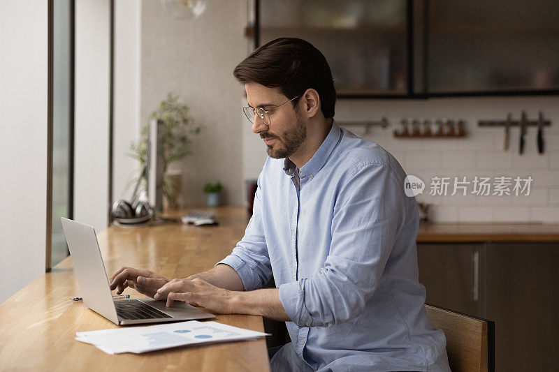 严肃的男性企业家坐在桌子旁用笔记本电脑工作
