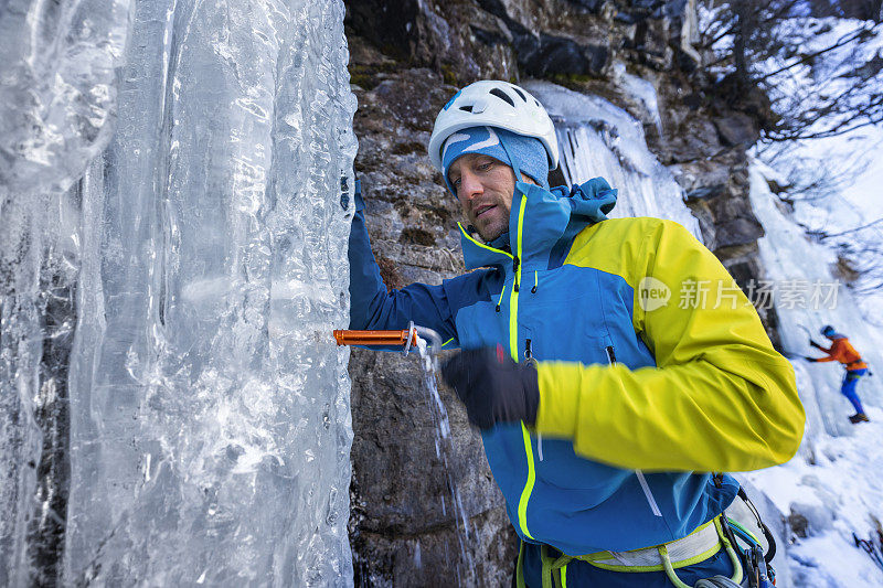 冰攀者在冰冻的瀑布中转动冰螺钉