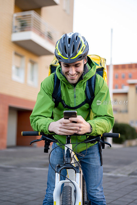微笑的年轻人骑自行车送箱子、文件和食物回家，快递员利用智能设备技术查找地址和发送工作报告