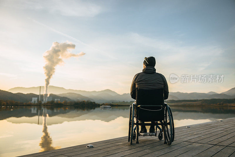 瘫痪的人坐在轮椅上，在湖边的码头上看日落