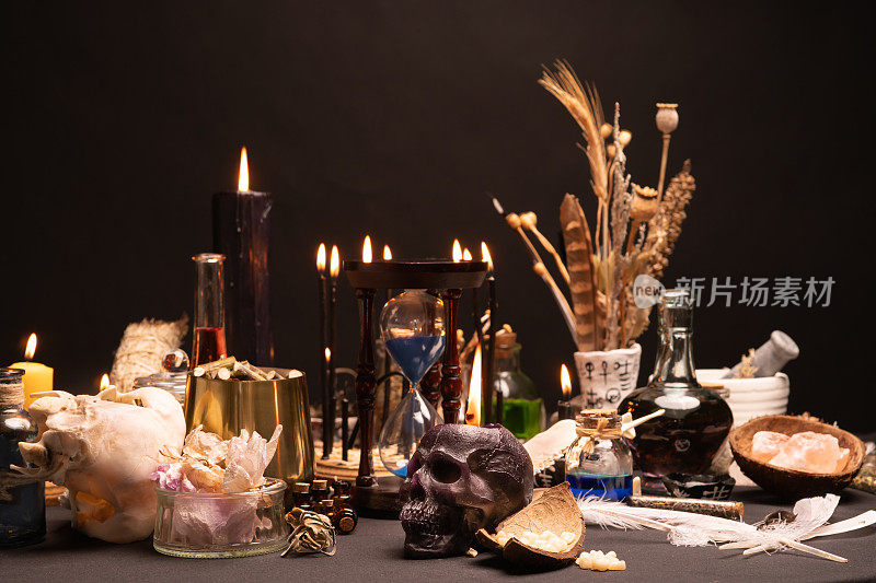 选择性聚焦于人类头骨蜡烛。神秘和深奥的巫医静物。万圣节的魔法物品。黑蜡烛，水晶石，牙齿药水瓶在女巫的桌子上。神秘的巫术。