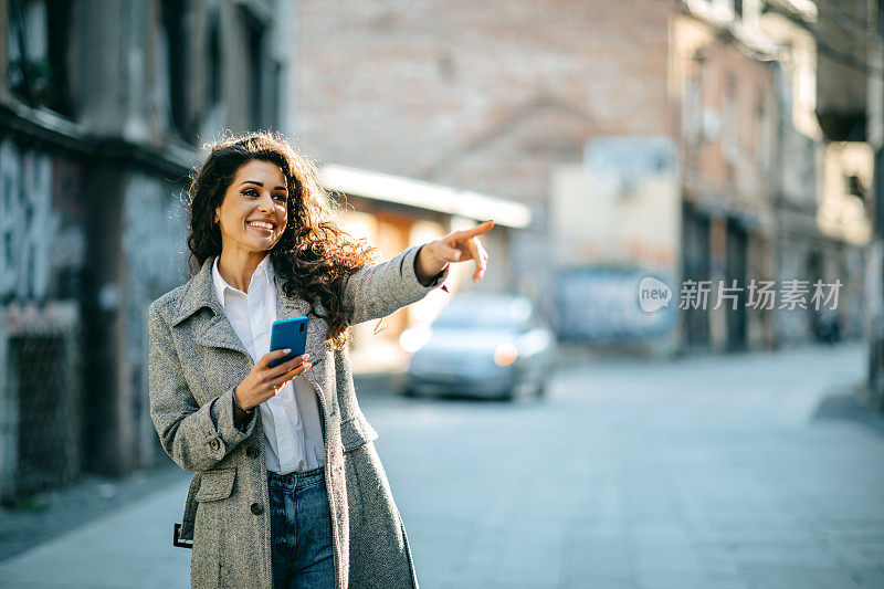 女人在户外用手机聊天，穿着西装的职业女人走在老城的街道上检查她的智能手机