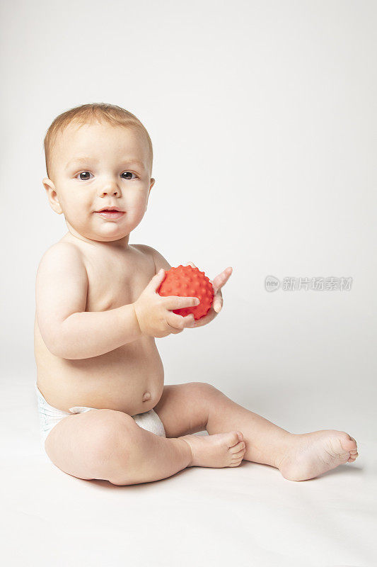 9个月大的小男孩穿着尿布抱着小红球