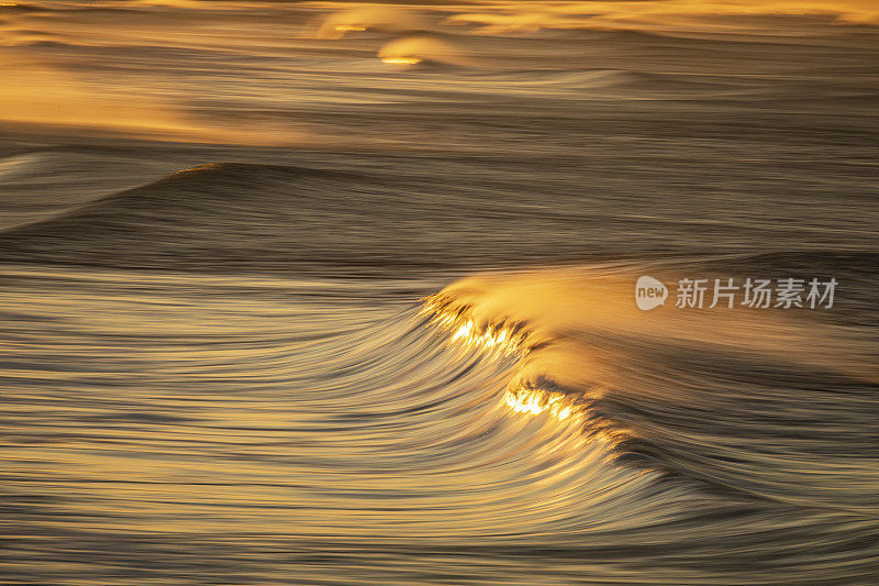 清澈的海浪在沙滩上反射出明亮的金色日出