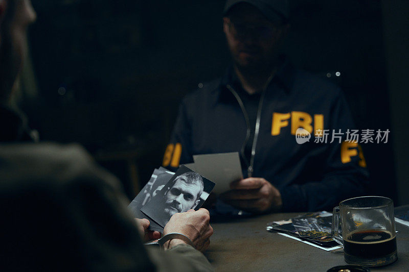 一名警官和一名嫌疑人在黑暗的审讯室里的动作电影场景，我们看到了嫌疑人手里的照片