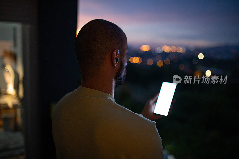 男子商人在黄昏时在家中阳台上使用手机