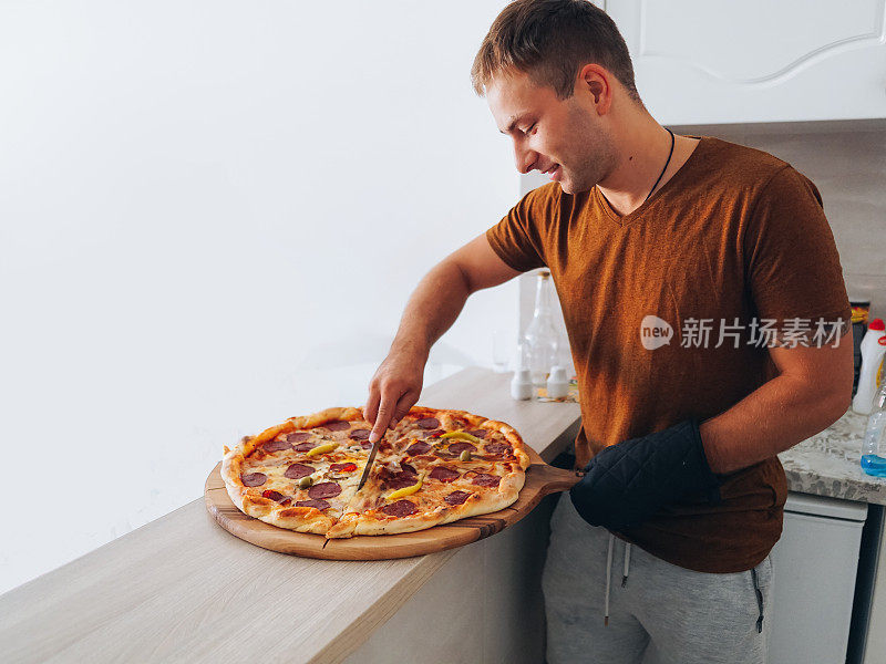 男子在厨房准备披萨，从烤箱取出披萨和服务