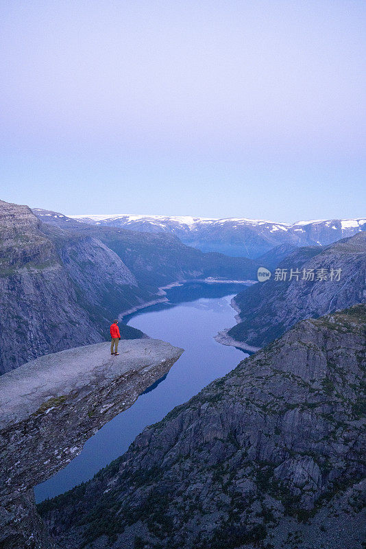 男性徒步旅行者站在巨魔之舌(trollltunga)著名的岩石上，俯瞰湖面上的山谷全景，是挪威著名的探险之旅