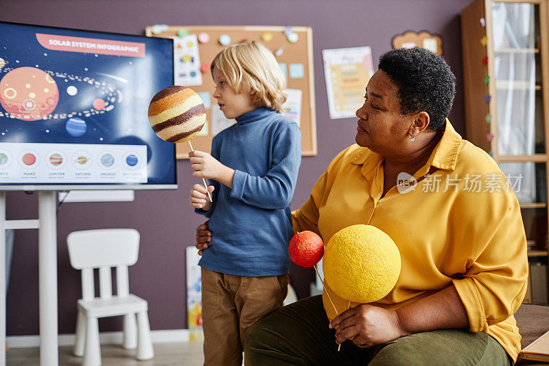 成熟的幼儿园老师和小男孩与行星模型