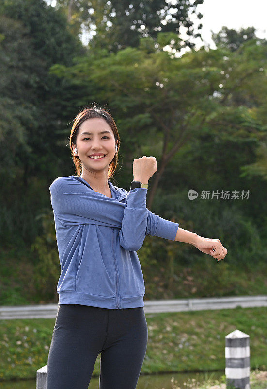一名穿着运动服的亚洲女子在早上的公园跑步前伸展手臂热身。
