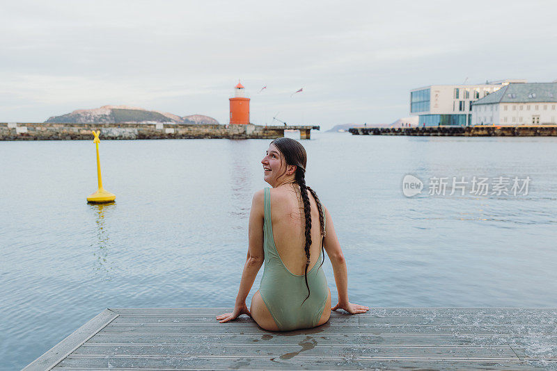 女性在泳装坐在码头上看红色灯塔在Norwa的后视图
