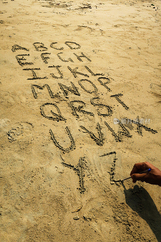 图像无法识别的人在沙滩上用圆珠笔在阳光沙滩上用方块大写字母书写字母，高视图，重点在前景