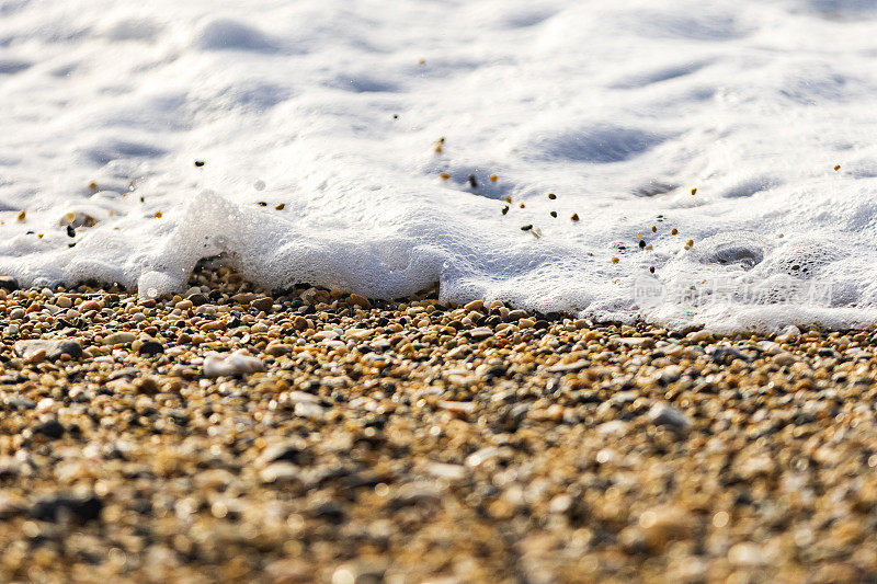 特写白色的泡沫海浪冲刷着海滩上的小鹅卵石