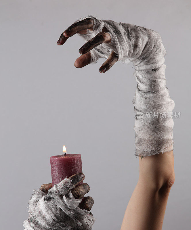 裹着绷带的木乃伊手拿着黑色背景上燃烧的蜡烛。万圣节的概念
