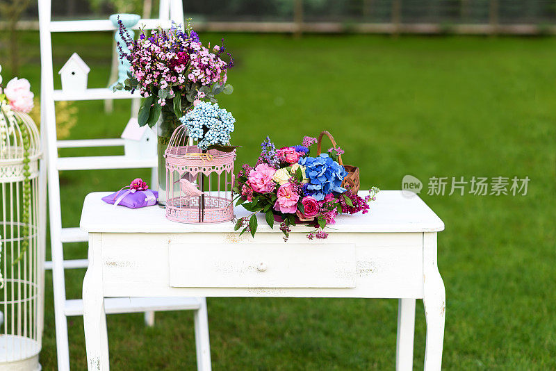 复古的婚礼装饰，白色的桌子，鲜花和鹦鹉笼。