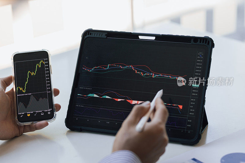商人工作在平板电脑和智能手机分析股票市场投资图表。投资者在移动和平板电脑应用程序上分析股市和外汇交易图表数据。