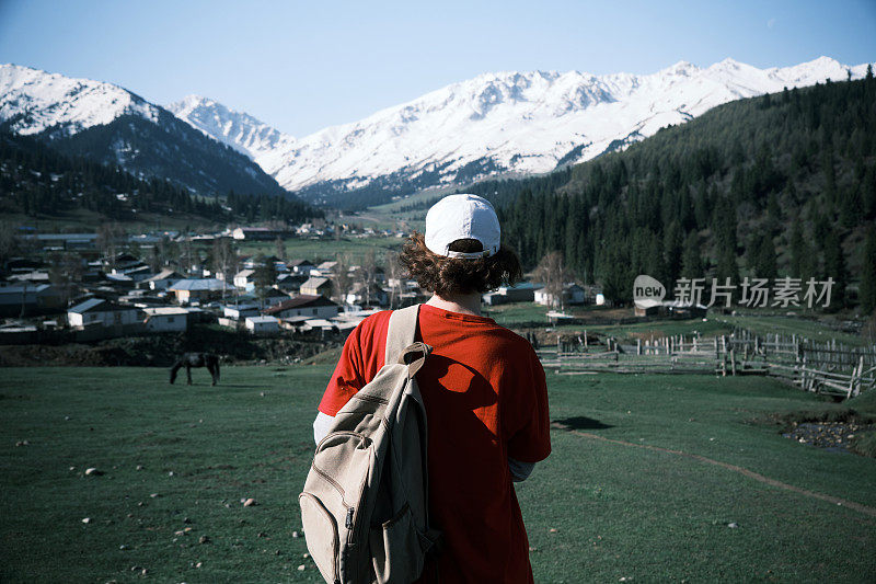 一位女背包客正从山坡上眺望山村