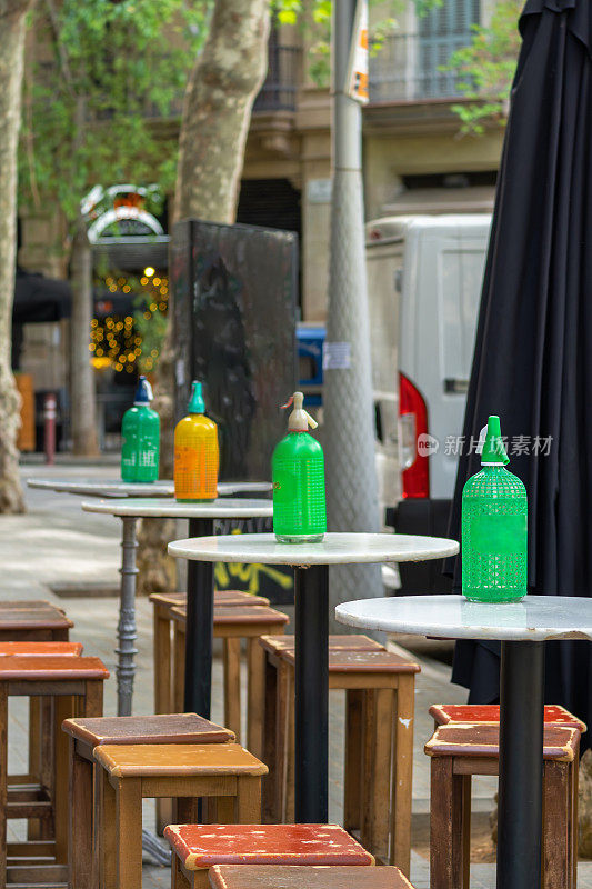 在巴塞罗那一家古色古香的老酒吧的露台上，小圆大理石高桌上摆放着古董和复古的橘黄色和绿色塑料网状虹吸管，上面放着苏打水，上面放着苦艾酒。