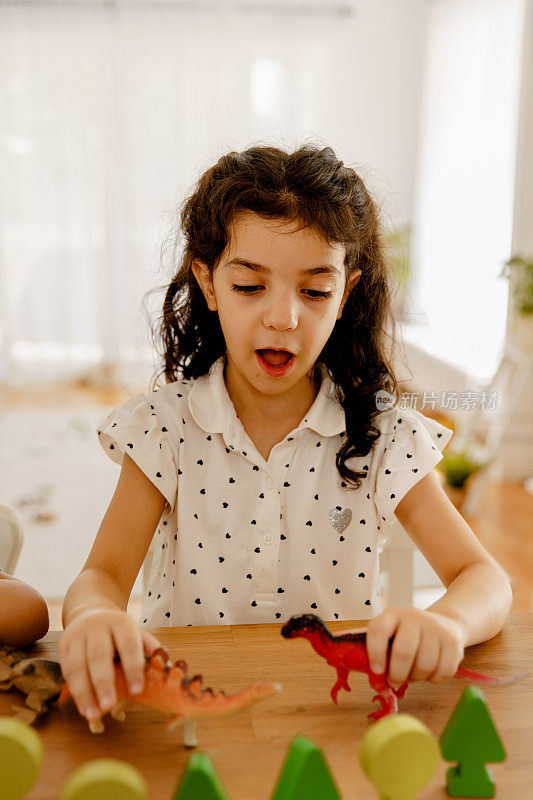 小女孩在家里的桌子上玩恐龙玩具