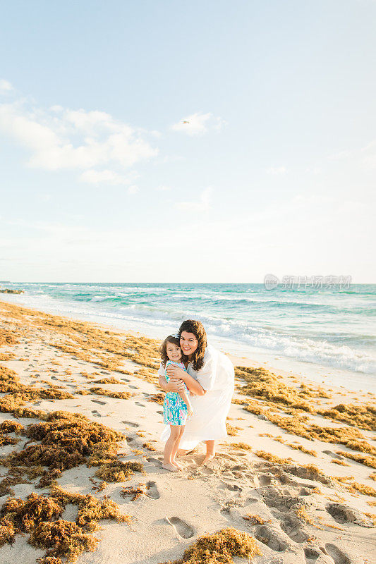 2023年春天，佛罗里达州棕榈滩，一位31岁的古巴裔美国母亲穿着白色及地长裙和她4岁的女儿一起走在沙滩上，在金色的日出中一起享受时光