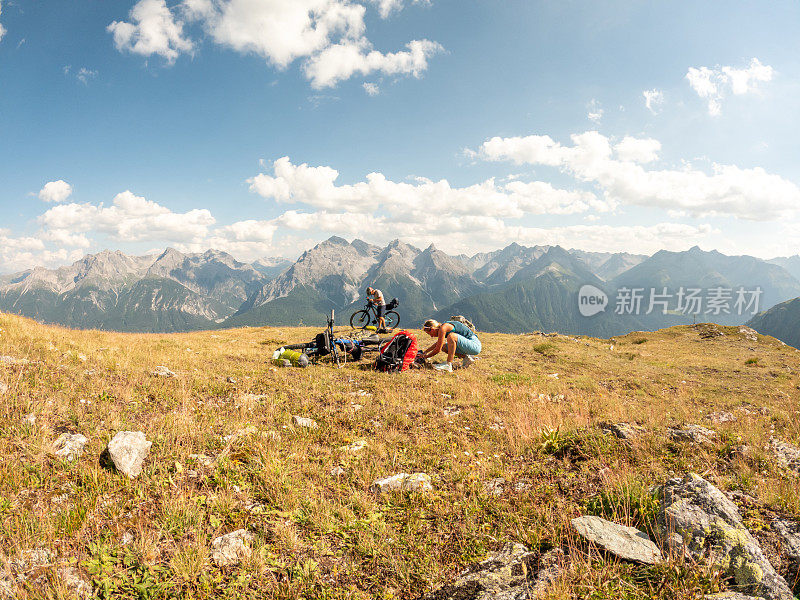 一对夫妇在瑞士阿尔卑斯山骑自行车，日落时分在山顶搭起帐篷