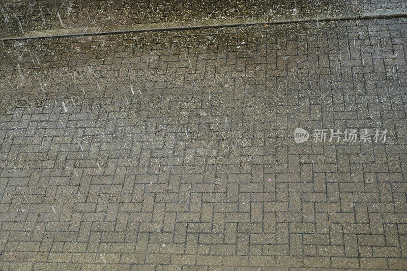 倾盆大雨落在铺砌的地面上的向下视图。