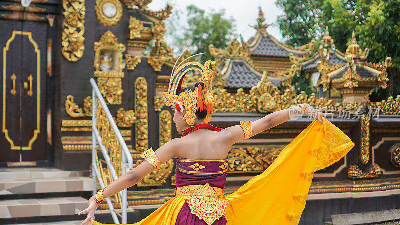 巴厘女孩穿着巴厘传统服装，以巴厘寺庙为背景，戴着王冠、珠宝和黄金饰品，做着舞蹈动作
