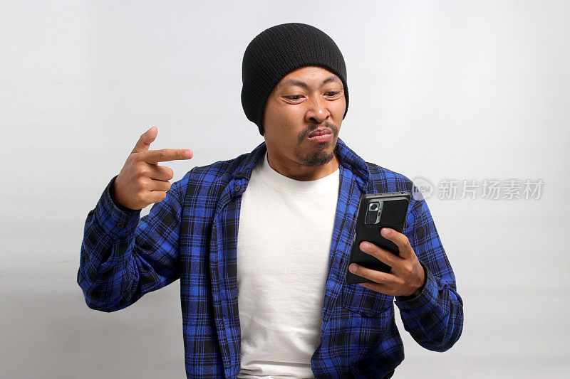 一名愤怒的亚洲男子对坏消息的反应是指着自己的手机